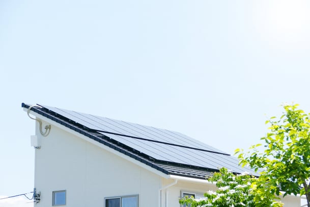 青空を背景に、住宅の傾斜した屋根に並べられた太陽光パネルの様子。