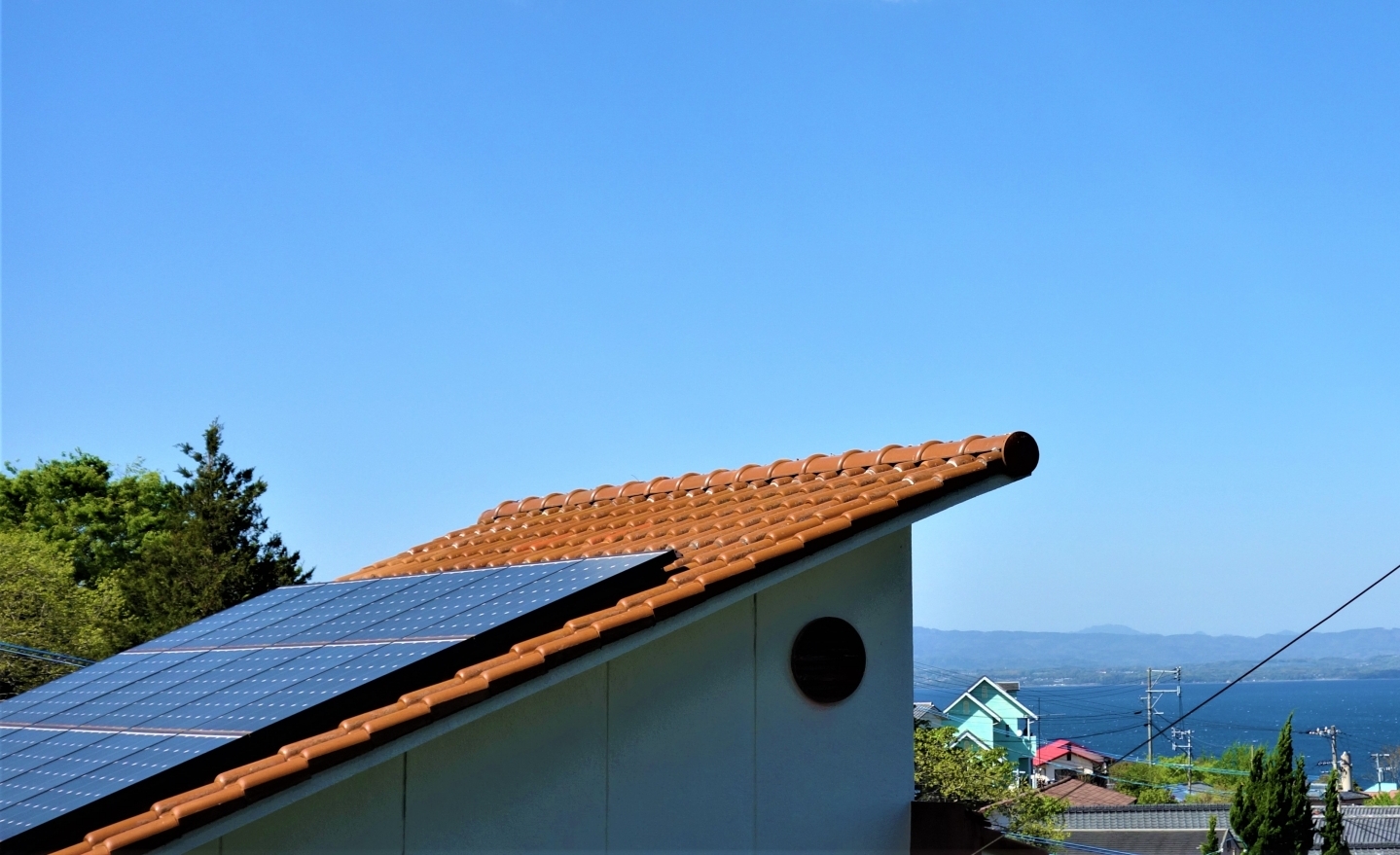 太陽光パネルの載った住宅屋根と青い空、海と緑