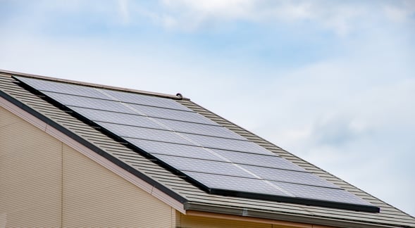 青空を背景に、住宅の屋根いっぱいに設置された太陽光パネルの様子。